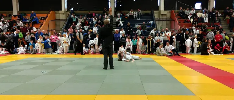 A Judo referee raising one arm above the head to signal ippon between two competitors