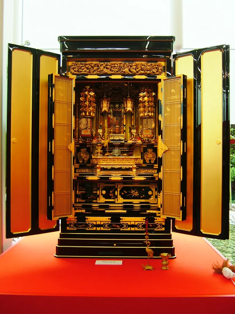Open Japanese butsudan with a gilded interior, ritual vessels, and a central Buddhist image