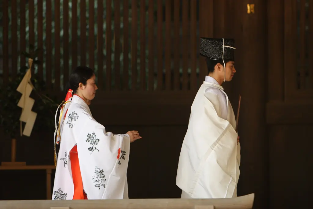 Shinto priests in white robes and black hats standing with red-and-white-clad miko at Meiji Jingū
