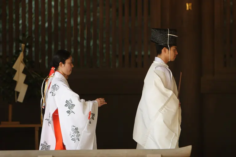 Shinto priests in white robes and black hats standing with red-and-white-clad miko at Meiji Jingū