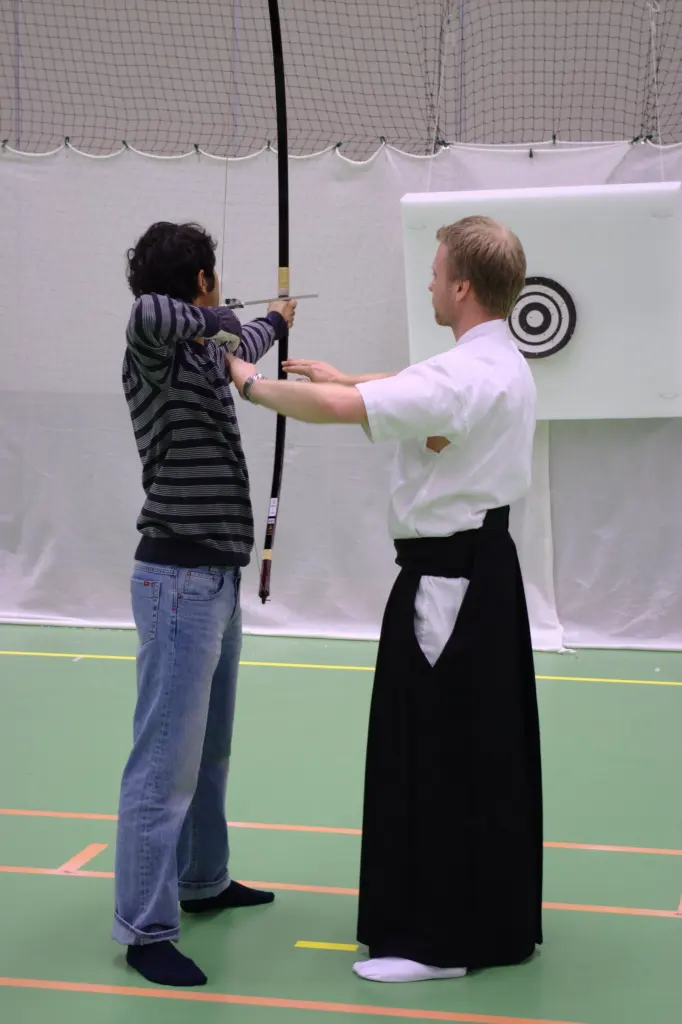 Kyudo practitioners holding long asymmetric Japanese bows at an outdoor shooting line