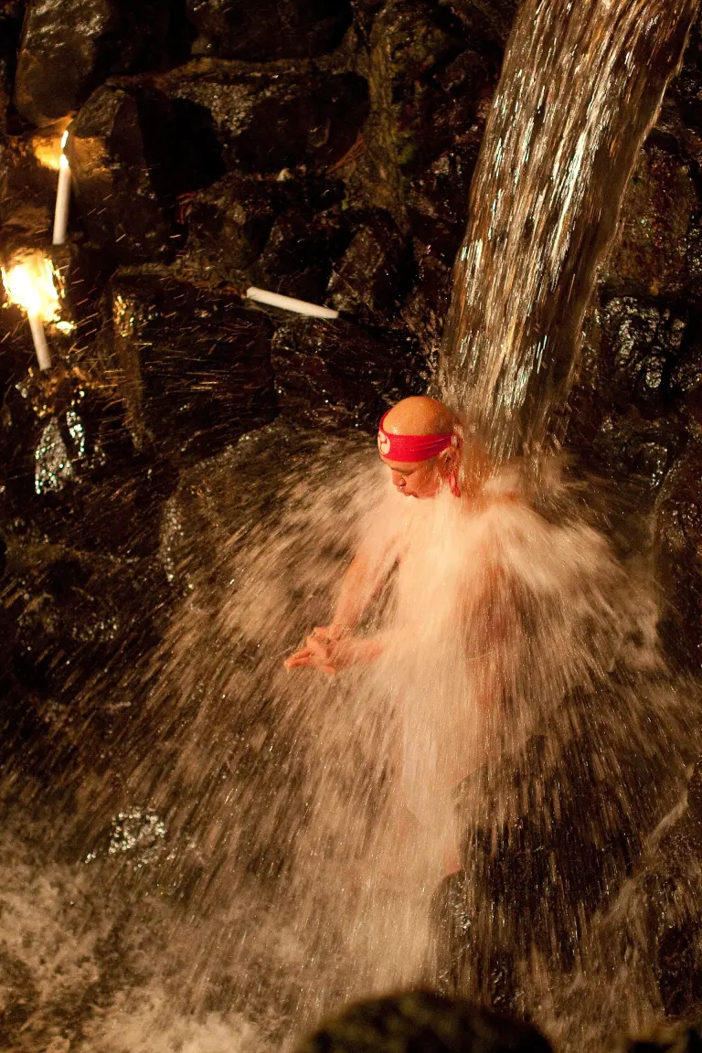 White-clad participants standing beneath a waterfall during supervised misogi-harai