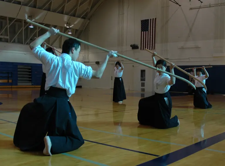Naginata practitioners holding long training weapons in a coordinated demonstration pose