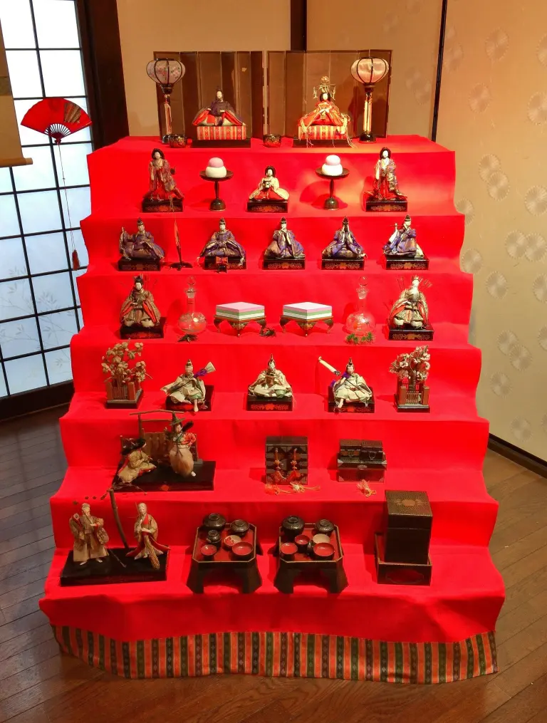 Seven tiers of Hina Matsuri dolls and miniature court furnishings on red cloth