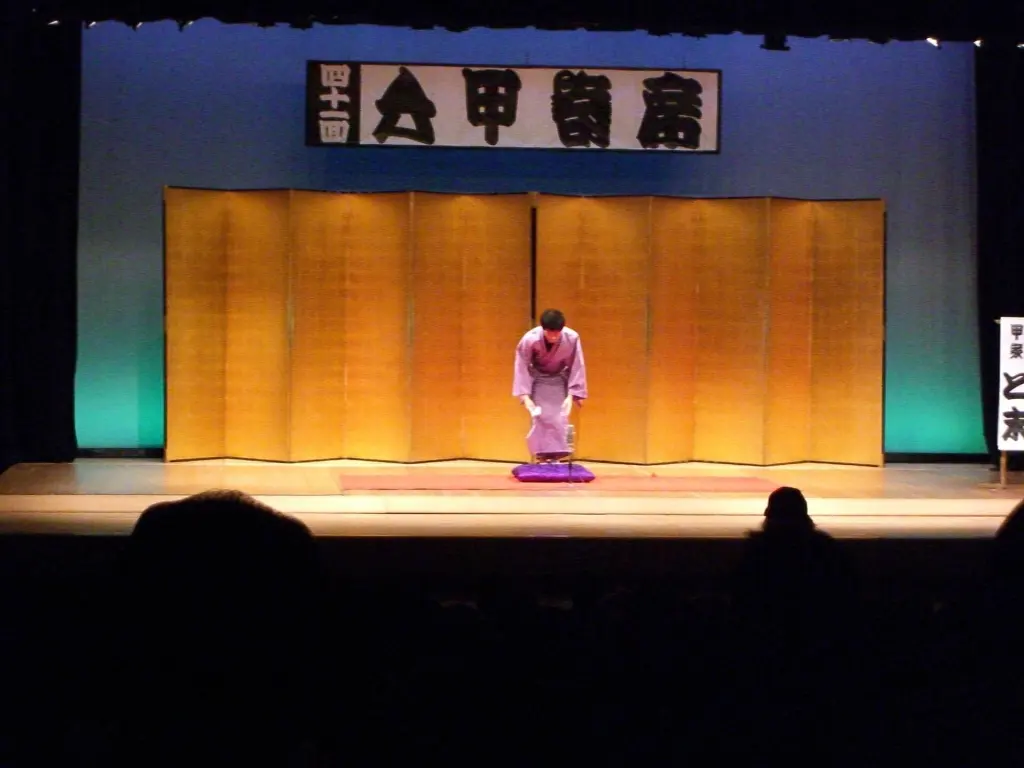 Rakugo storyteller in kimono bowing on a stage cushion