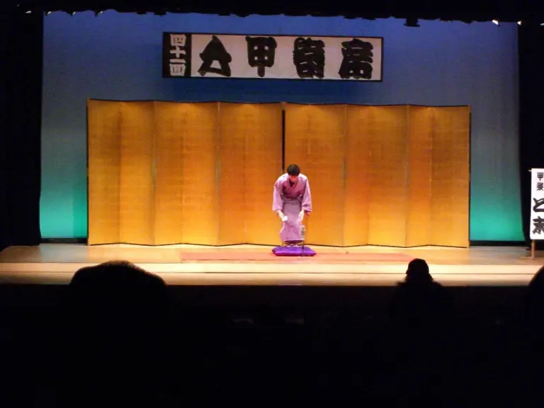Rakugo storyteller in kimono bowing on a stage cushion