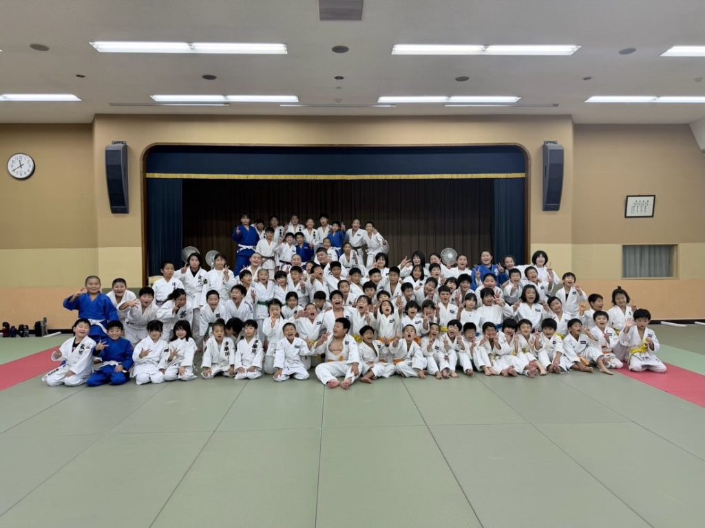 Young judoka and adults gathered on the tatami at the Tokai University Tsumagoi judo camp