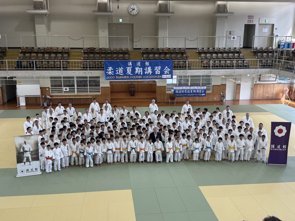 Participants in judogi gathered beneath the summer course banner inside the Kodokan dojo