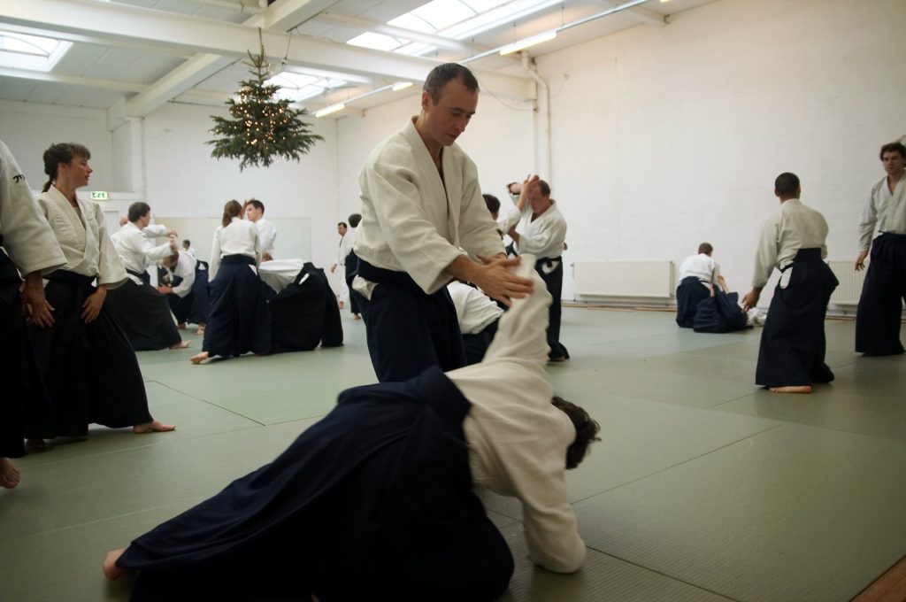 Aikido practitioners training an arm-lock takedown in a dojo