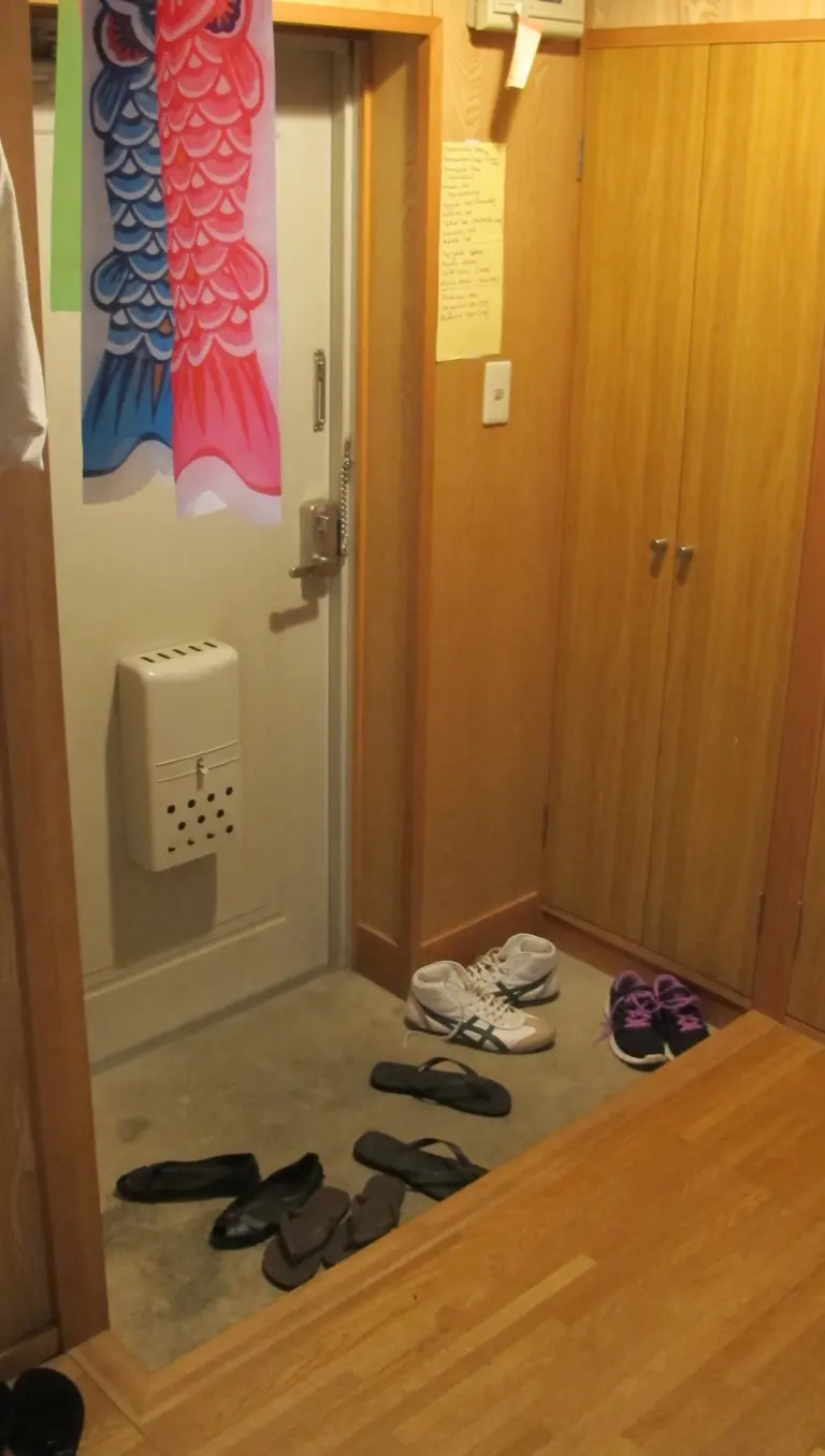 Narrow Japanese apartment entryway with shoes below a raised wooden floor
