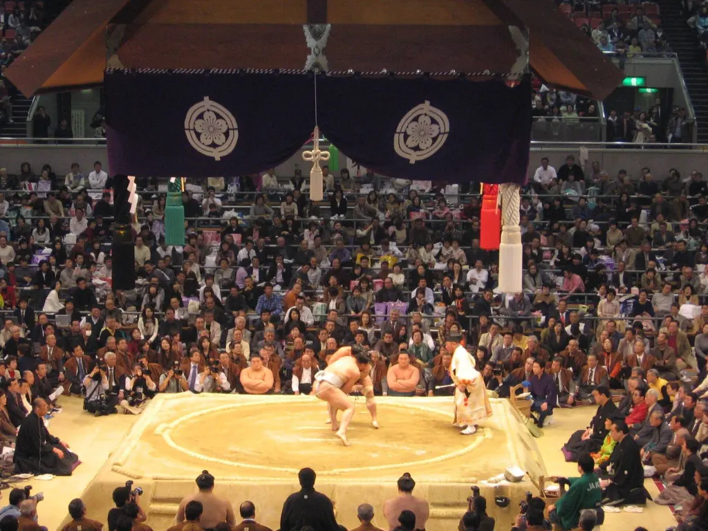 Raised clay sumo dohyō with a straw-bale circle beneath a suspended roof at the 2006 Osaka tournament