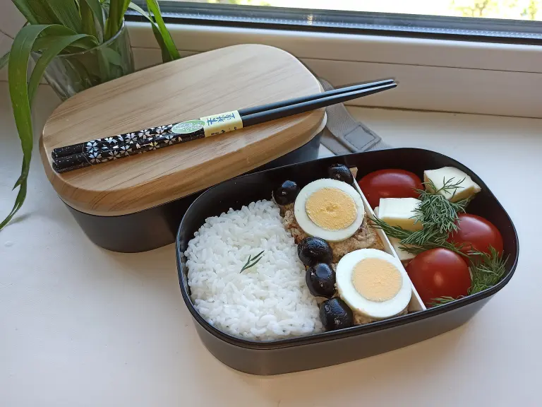 Open bento box with rice, vegetables, egg, and other side dishes