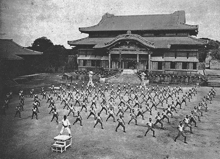 Black-and-white photograph of karate practitioners training outdoors before Shuri Castle