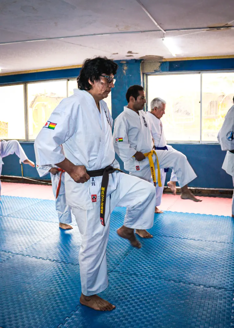 Karate practitioners perform kihon balance and posture exercises in a dojo