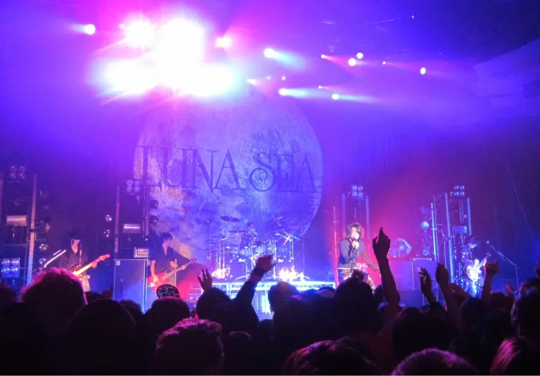 LUNA SEA perform under purple and blue lights at the Hollywood Palladium with the band's moon backdrop behind them