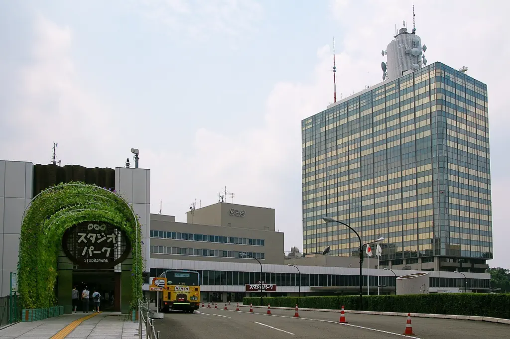 The multi-storey NHK Broadcasting Center seen from a tree-lined street in Shibuya