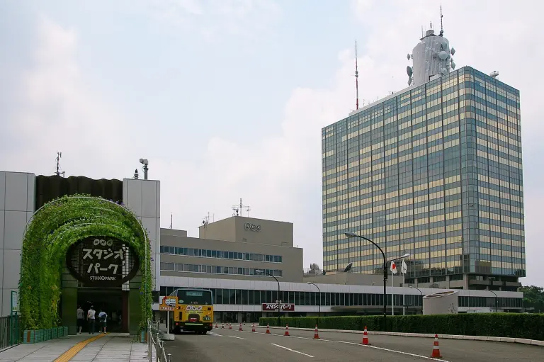 The multi-storey NHK Broadcasting Center seen from a tree-lined street in Shibuya