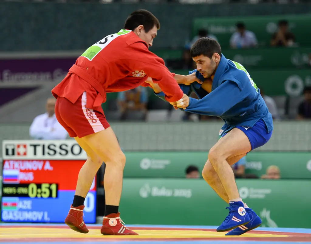 Two Sambo athletes in red and blue jackets grappling during the 2015 European Games