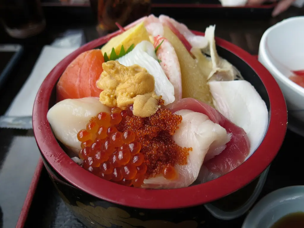 Bowl of rice topped with sliced fish, salmon roe, sea urchin, and garnishes
