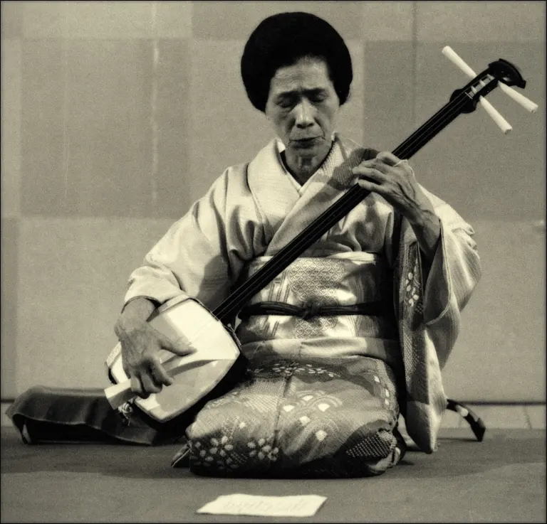 A musician holding and playing a shamisen.