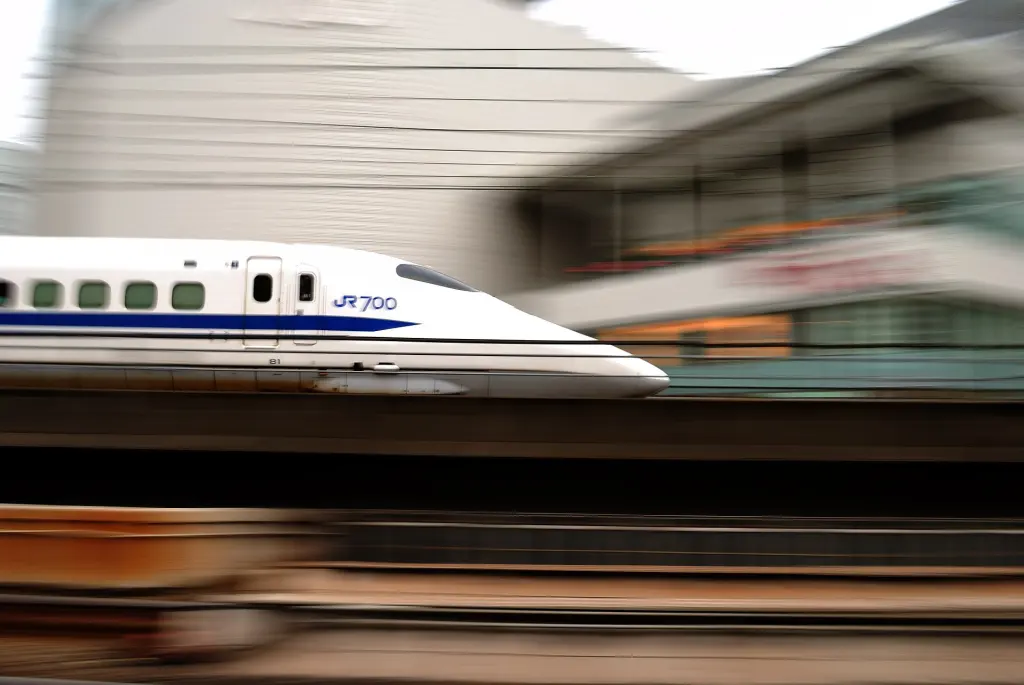 White and blue Shinkansen train passing beneath city buildings in Tokyo