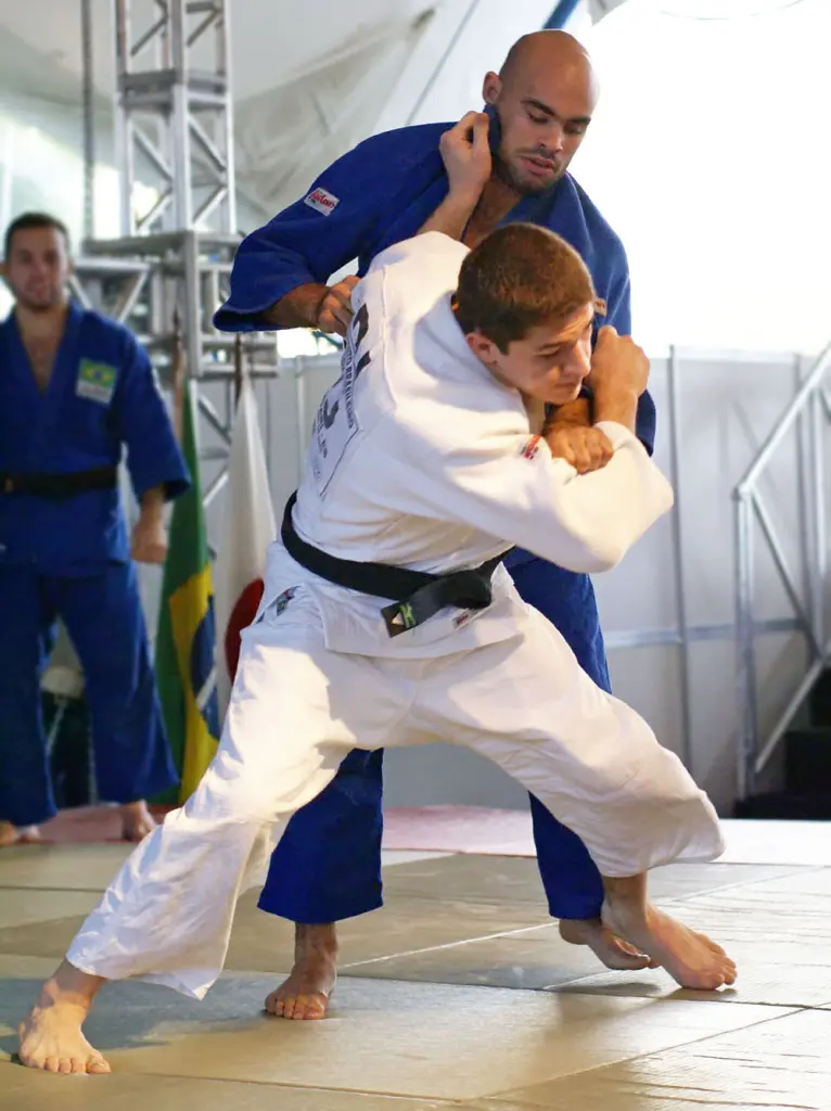 Two judoka demonstrate tai-otoshi on a mat