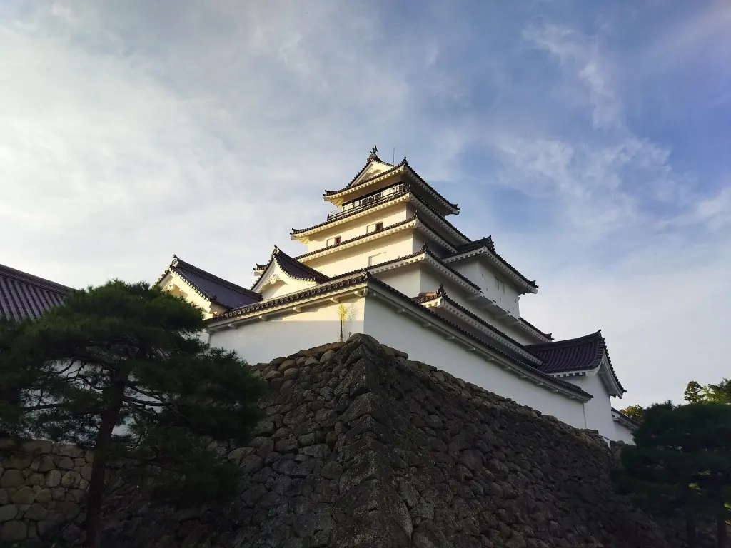 White reconstructed keep of Tsuruga Castle behind stone walls and trees under a blue sky