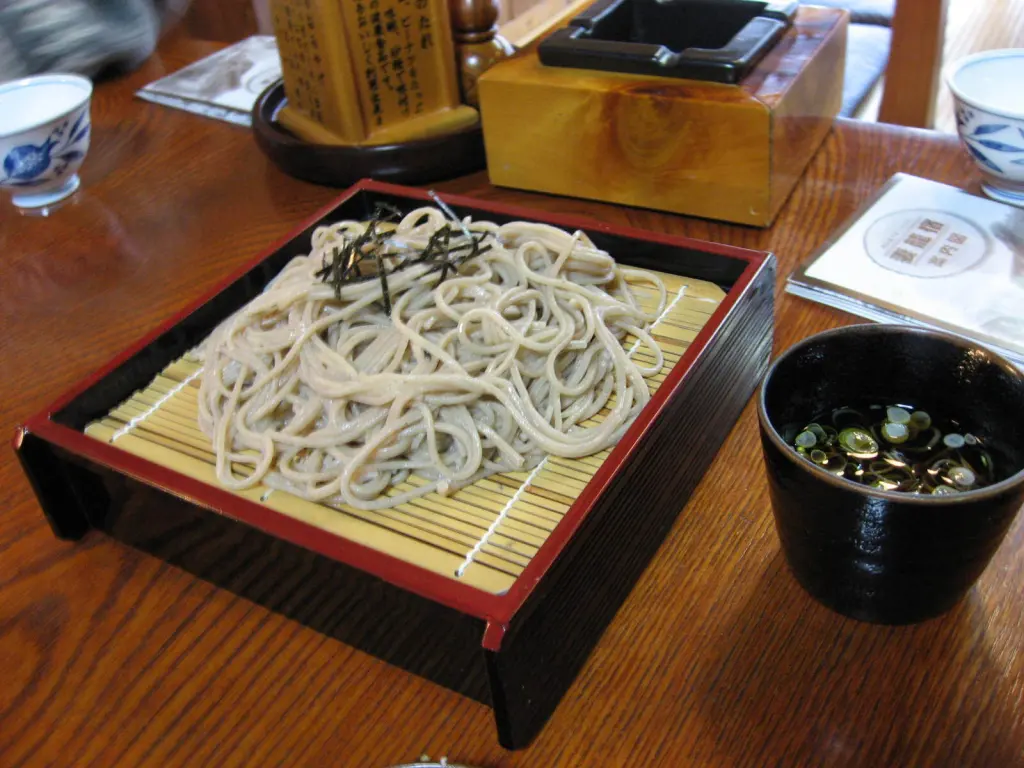Chilled soba noodles on a bamboo tray with a cup of dipping sauce
