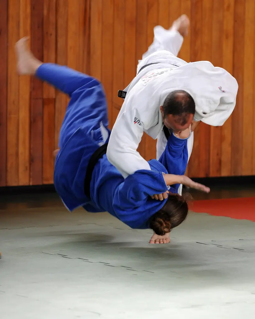 Two judoka in a training camp completing a controlled throw on the mat