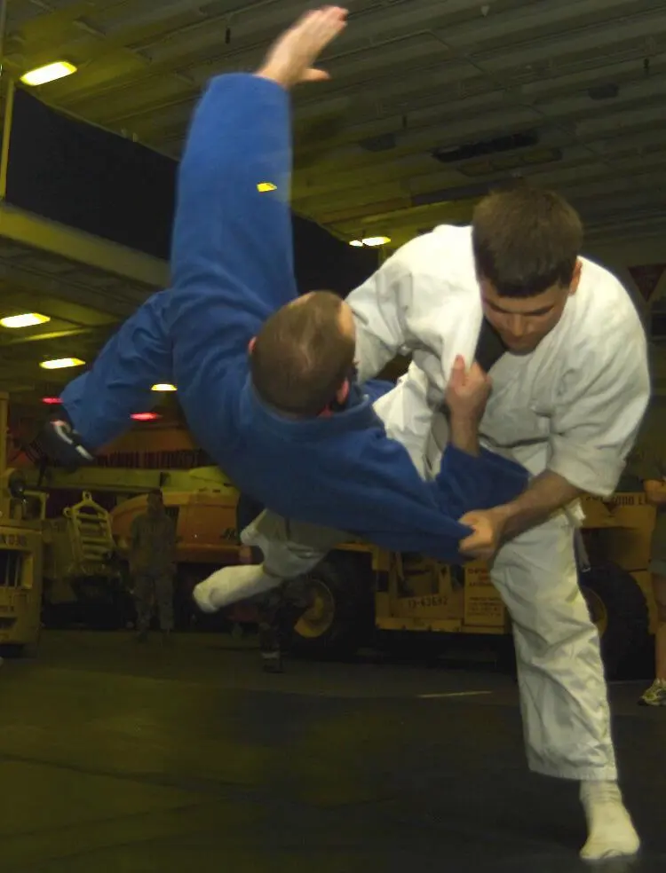 Two Judo practitioners moving through a throw on a mat