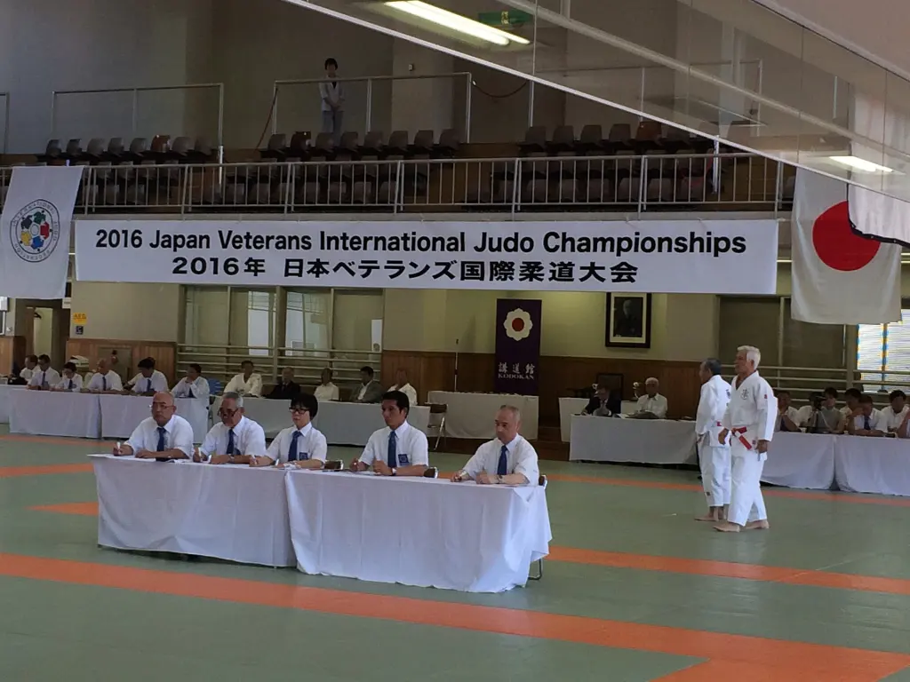 Two judoka performing a paired kata on a competition mat before judges