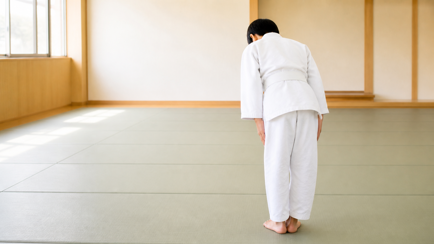 A young judoka bows at the edge of a tatami dojo before practice.